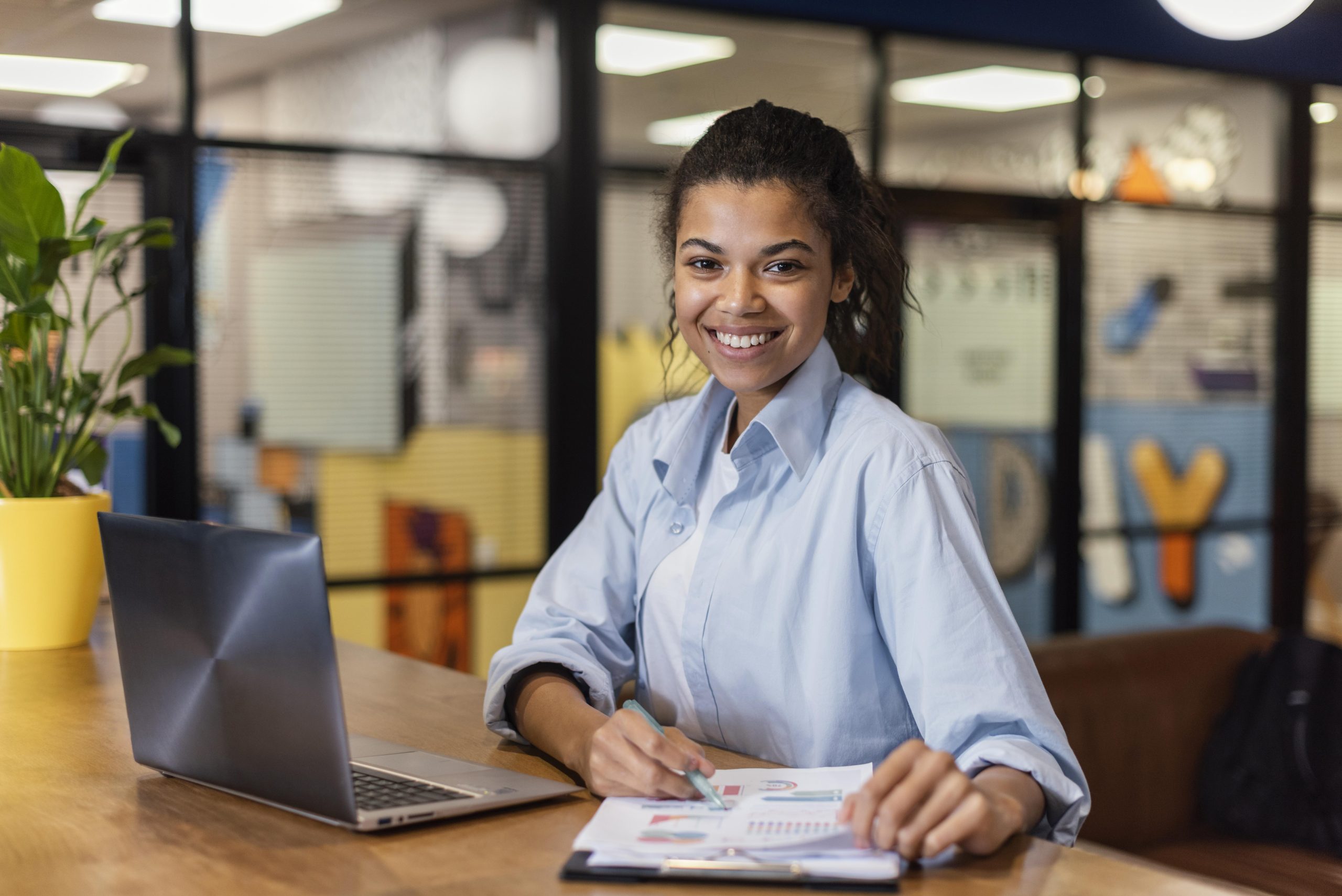 jovem trabalha sentada em uma mesa de escritório diante um notebook e algumas planilhas