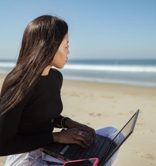 Uma mulher está na praia com o notebook no colo em uma das Melhores Cidades para Emprego de Verão em 2023