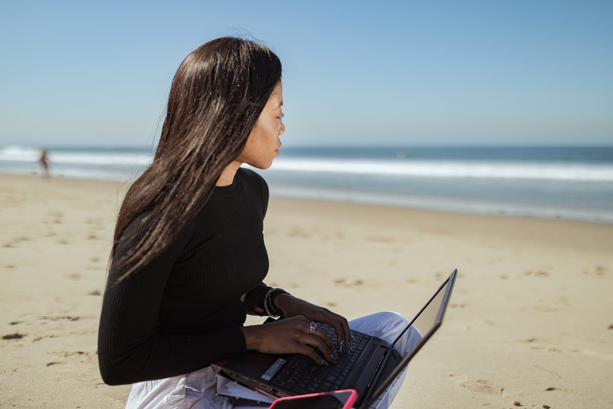 Uma mulher está na praia com o notebook no colo em uma das Melhores Cidades para Emprego de Verão em 2023