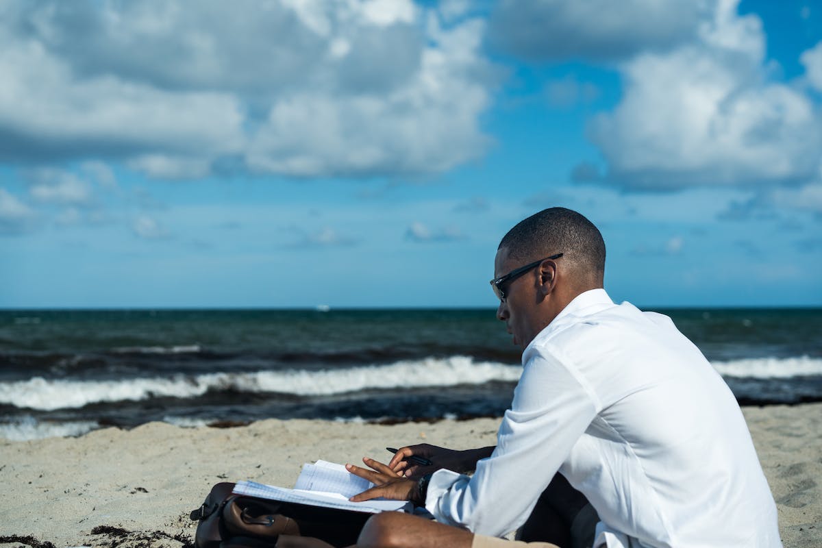 Um homem está na praia com o caderno no colo em uma das Melhores Cidades para Emprego de Verão em 2023