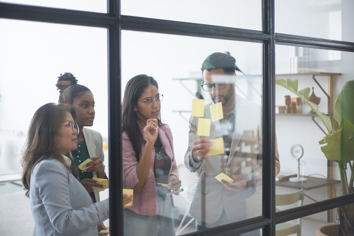 Um grupo de mulheres está vendo as informações que o seu supervisor está colando em uma parede de vidro no escritório 