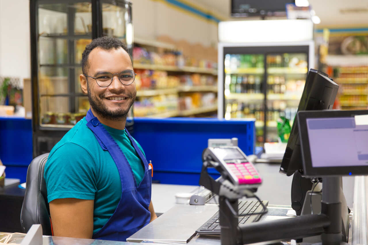 Caixa de supermercado posa sorridente em sua posição de trabalho