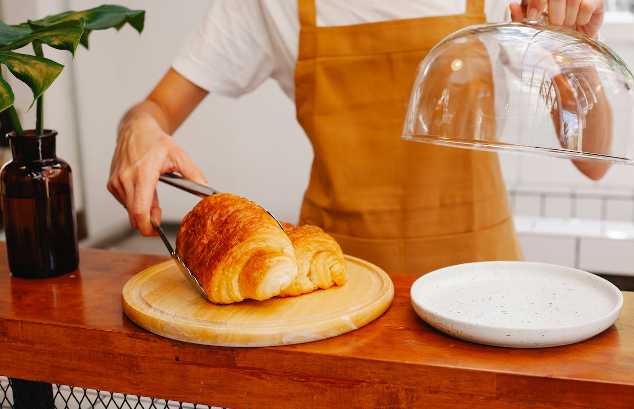Uma jovem aprendiz que trabalha na padaria está pegando um pão com um pegador