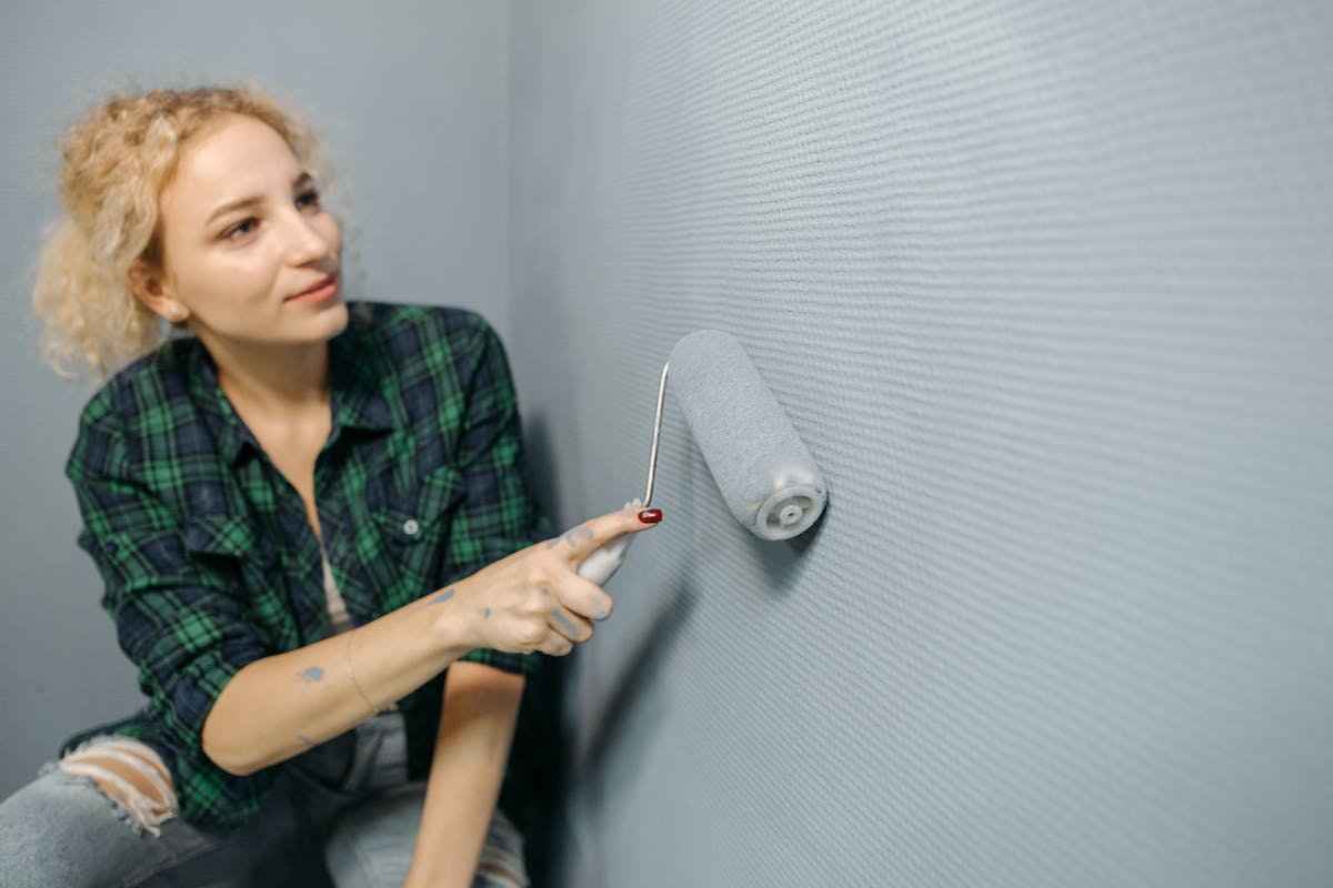 Uma mulher está pintando a parede de cinza com um rolo de tinta. Ela foi aprovada no Jovem Aprendiz Hortolândia 2024